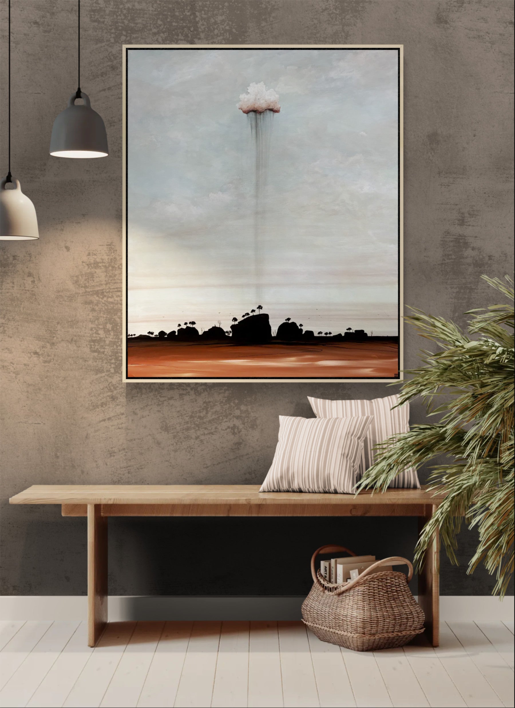 A framed landscape art original painting hangs on a textured gray wall above a wooden bench with striped pillows and a woven basket. The artwork depicts a dramatic cloud formation over a dark silhouetted landscape, with a muted blue-gray sky and a rust-brown horizon.