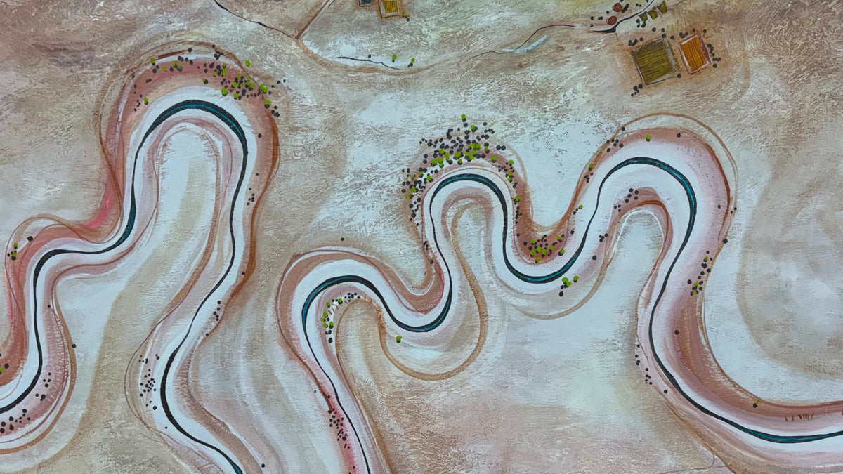 Aerial view of a winding desert landscape with pale pink and beige rock formations, dark blue-green river channels, and small clusters of green trees.