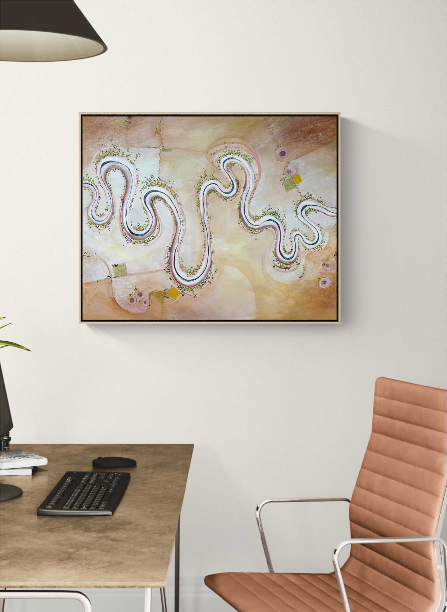 Abstract framed wall art hanging on a white wall above a desk, showing a winding multicolor snake-like line on a soft beige and peach background. A brown office chair and part of a desk are visible in the room.