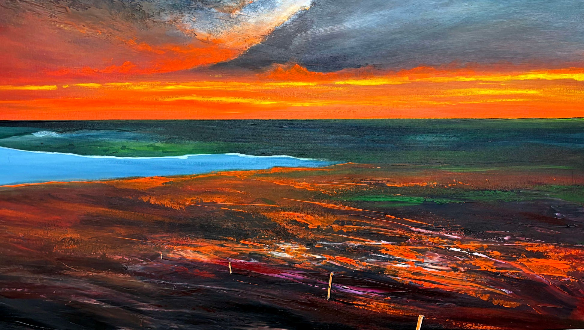 Sunset over a landscape with a body of water and a fence in the foreground.