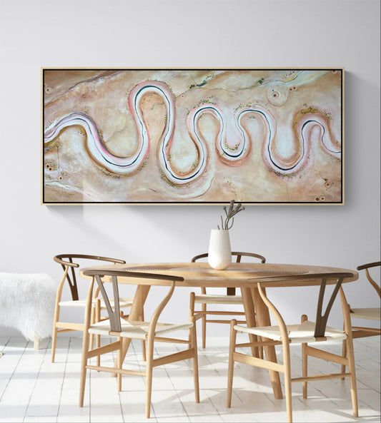 A large framed abstract wall art piece hangs above a wooden dining table and chairs in a bright, modern room. The artwork features flowing, wavy lines in cream, beige, blush pink, and soft blue tones.