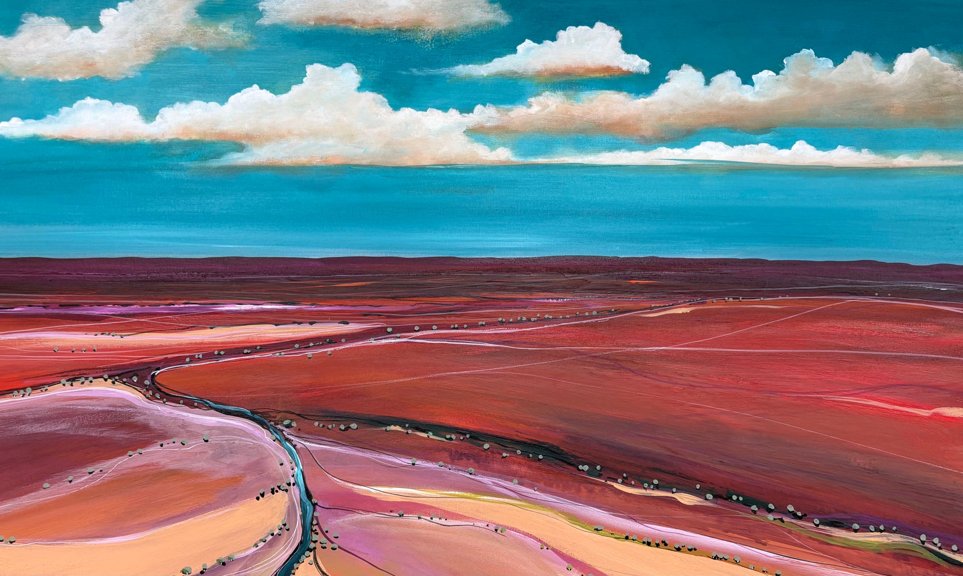 Aerial view of a colorful landscape with red and pink hues under a blue sky with clouds.