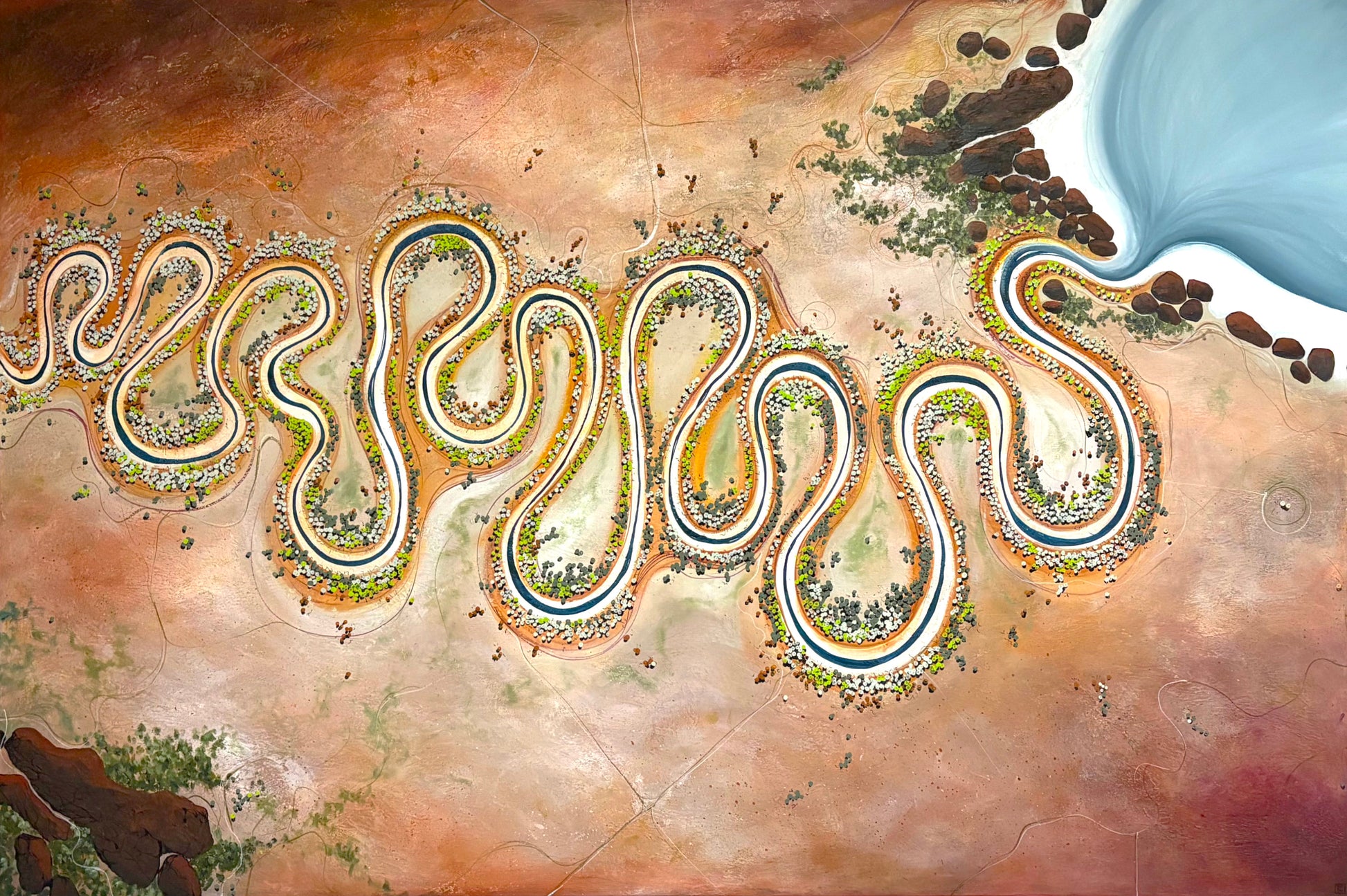 An aerial-style scenic artwork showing a winding blue river or road cutting through a warm tan and brown landscape with small green and yellow details, plus a pale blue body of water in the upper right.