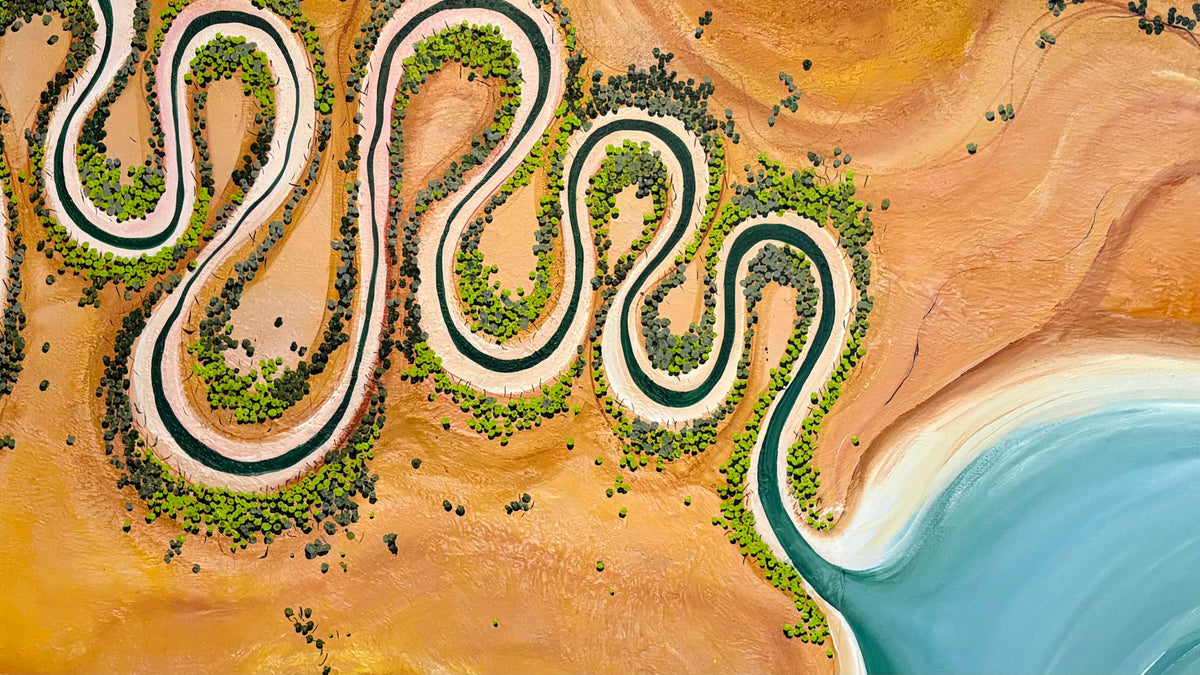 Aerial view of a winding river forming a serpentine S-shaped curve through a sandy orange desert landscape with green vegetation and a blue water body at the bottom right.